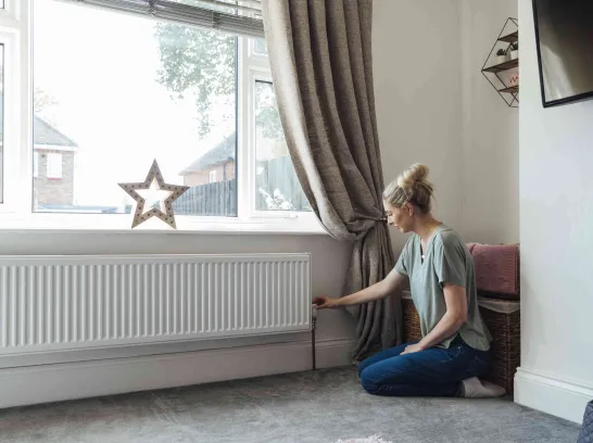 Frau dreht am Heizungsthermostat, um Energie zu sparen.