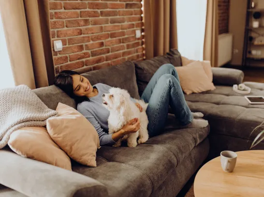 Frau liegt auf dem Sofa und streichelt ihren Hund