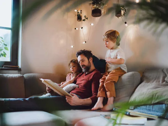 Ein Mann liest seinen Kindern unter einer Lichterkette vor.
