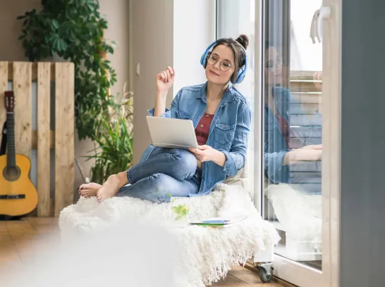 Eine Frau sitzt mit Kopfhörern und einem Tablet auf dem Schoß.
