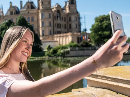 Eine Frau nimmt ein Selfie vor dem Schweriner Schloss von sich auf.