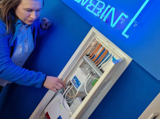 Eine Stadtwerkemitarbeiterin erklärt die Technik eines Medienschranks für das Glasfaser-Internet.