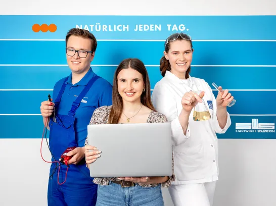 Drei Azubis der Stadtwerke Schwerin stehen vor einer blau gestreiften Wand.