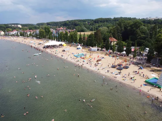 Luftaufnahme vom Zippendorfer Strand mit Festzelt und Kinderattraktionen. Zahlreiche Gäste am Strand und im See beim Baden.