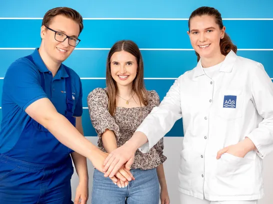 Drei Azubis stehen vor einer Wand.