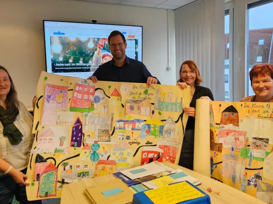 Vier Personen stehen in einem Büro uns halten Kinderbilder in die Kamera.