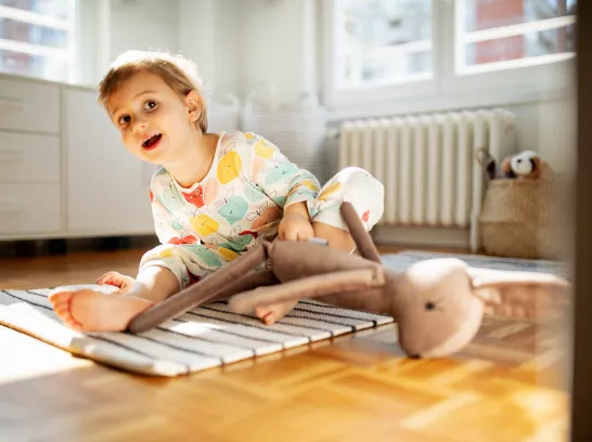 Ein Kleinkind sitzt mit nackten Füßen auf dem Fußboden.