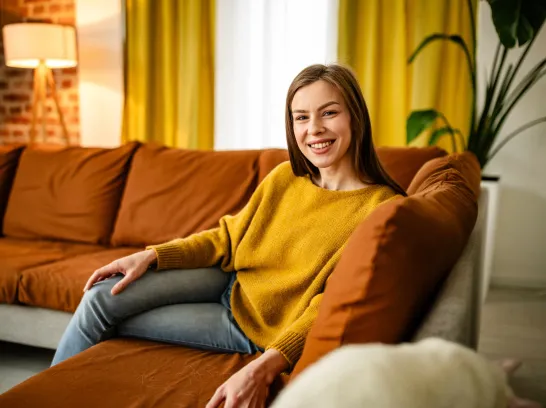 Eine Frau sitzt gemütlich auf dem Sofa und lächelt.