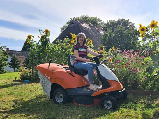 Frau sitzt auf einem Rasenmäher im Garten