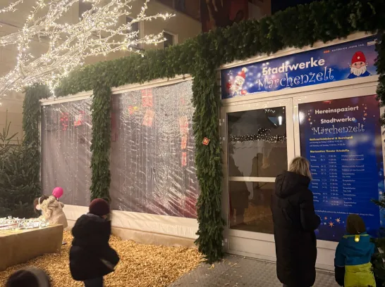 Ein kleine Familie schaut sich die Programmübersicht am Stadtwerke Märchenzelt auf dem Schweriner Weihnachtsmarkt an.