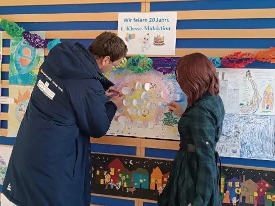 Ein Mann und eine Frau bestaunen bunte Kinderzeichnungenan einer Wand