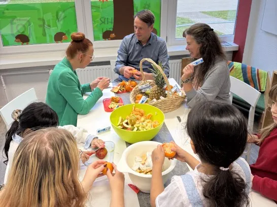 Kinder und Erwachsene sitzen an einem Tisch und schneiden gemeinsam Obst