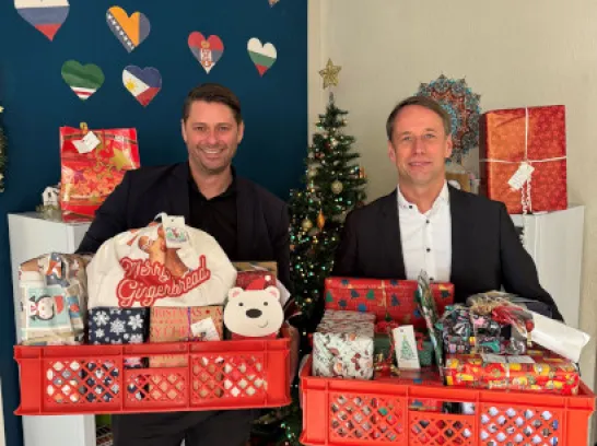 Zwei Männer stehen mit Geschenken vor einem Tannenbaum