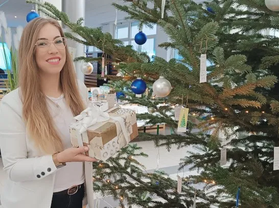 Eine junge Frau steht mit einem Geschenk neben einem Tannenbaum