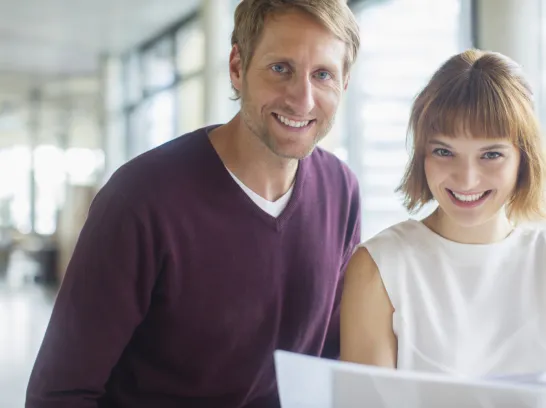 Ein Mann und eine Frau im Büro lächeln in die Kamera