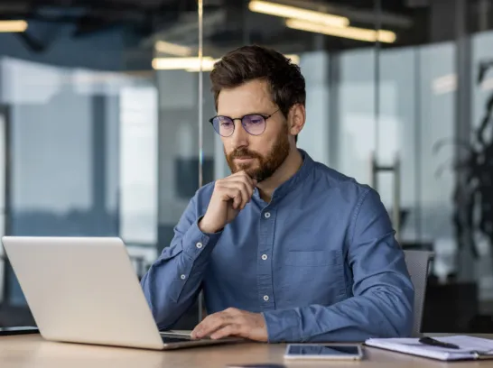 Mann schaut im Büro auf den Bildschirm eines Notebooks