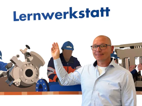 Ein gewerblicher Ausbildungsbetreuer steht vor einer gestalteten Wand