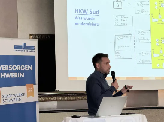 Mann steht mit Mikrofon in der Hand vor einer Präsentation und erklärt die Inhalte. 